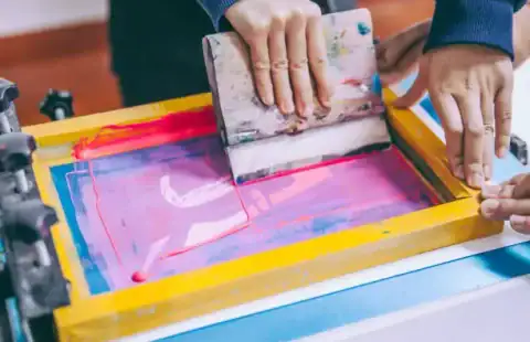 This image shows a screen printing plate being applied with ink using a squeegee during the screen printing process.