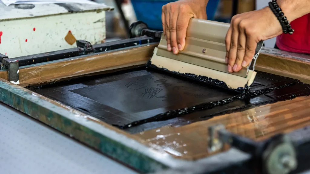 Serigrafi makinesi tavsiye rehberi için, ragle ile serigrafi kalıbına boya çekilerek baskı yapılan masa
